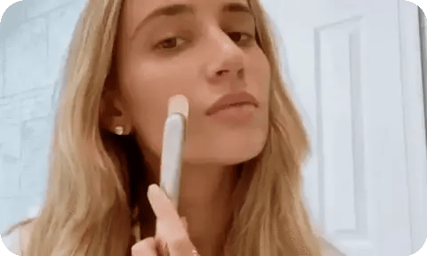 Woman applying makeup with a brush in front of a mirror