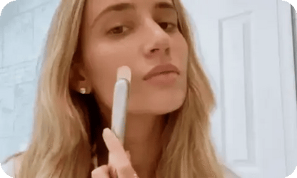 Woman applying makeup with a brush in front of a mirror